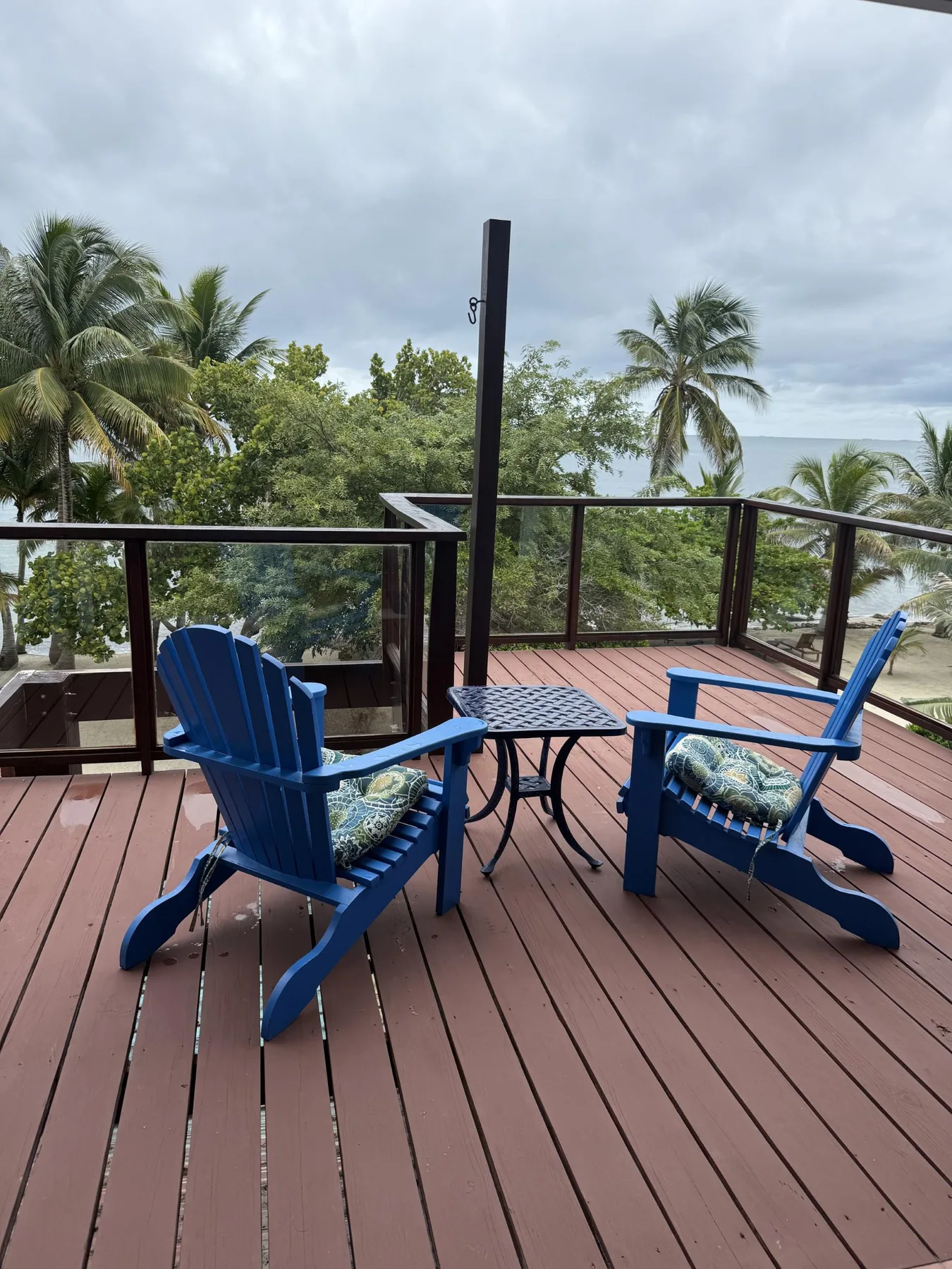 Una terraza con asientos azules y una mesa pequeña tiene vistas a palmeras y al agua.