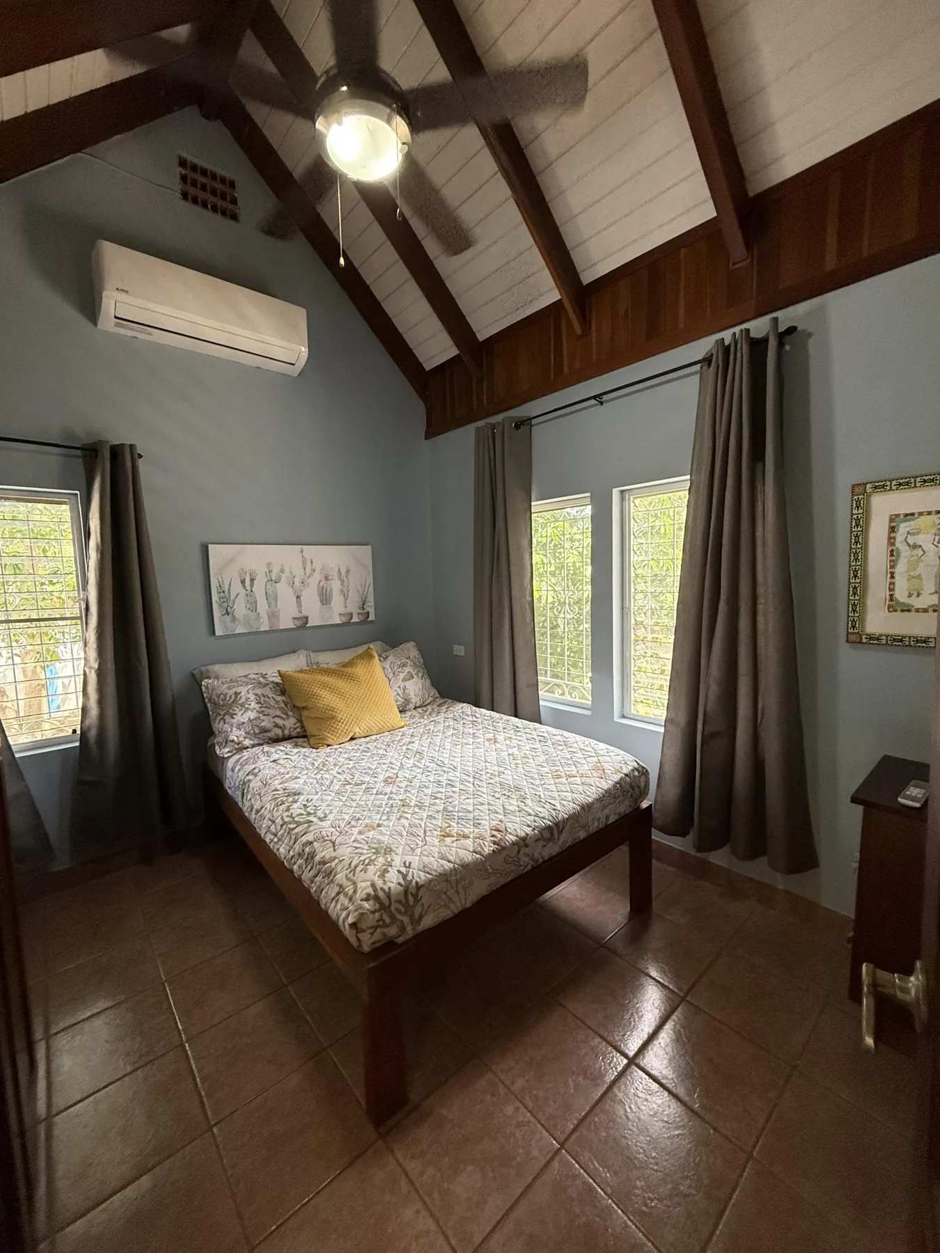 Un dormitorio con una cama bajo un techo alto con vigas y ventanas con cortinas.