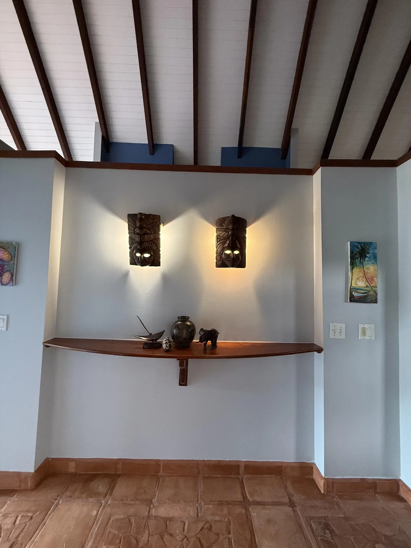 Una pequeña composición de pared muestra una repisa de madera, objetos decorativos y dos apliques iluminados.