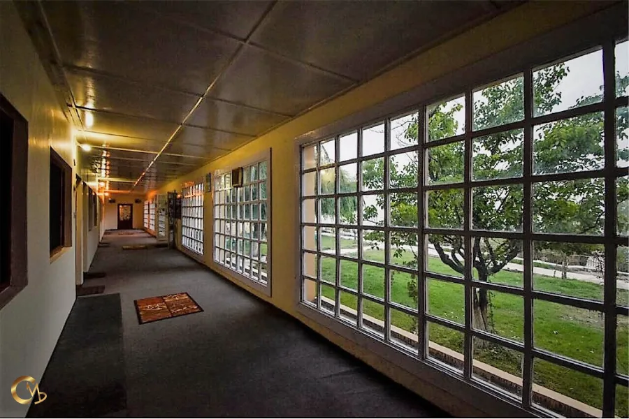 Espacio representativo del hotel: Un largo pasillo interior tiene grandes ventanas cuadriculadas que dan a un césped verde.