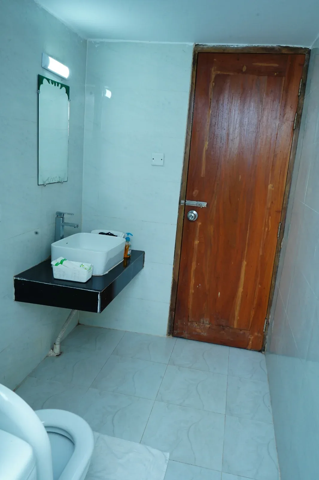 Representative hotel space: A tiled bathroom with a sink, mirror, and wooden door.