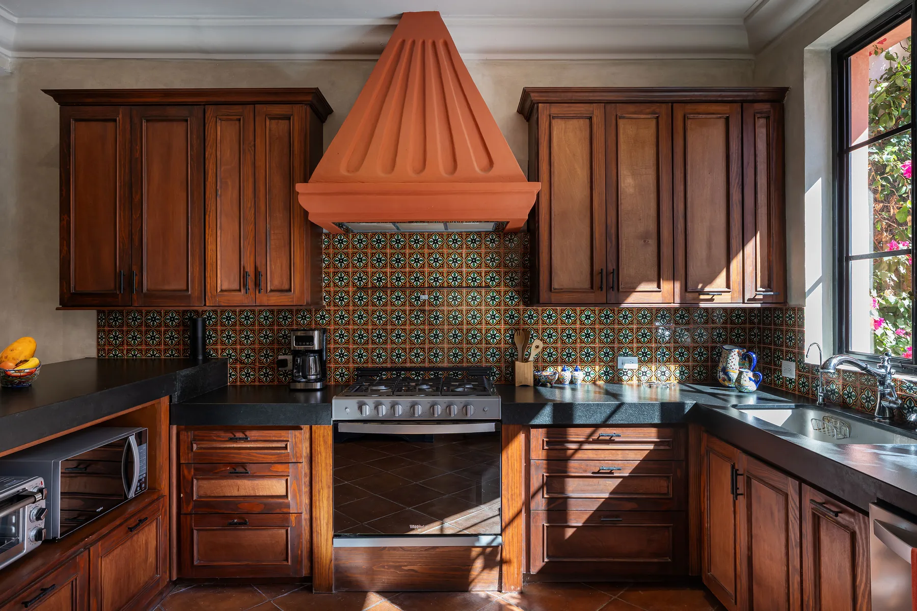 A kitchen with dark wooden cabinets, a tiled backsplash, and a central range hood.
