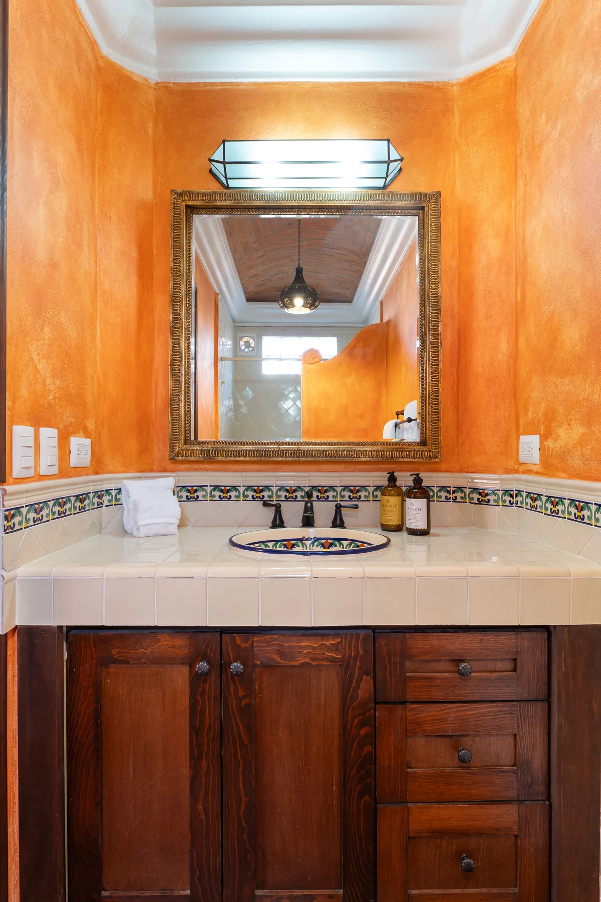 A bathroom vanity with a tiled counter, sink, and large wall mirror.