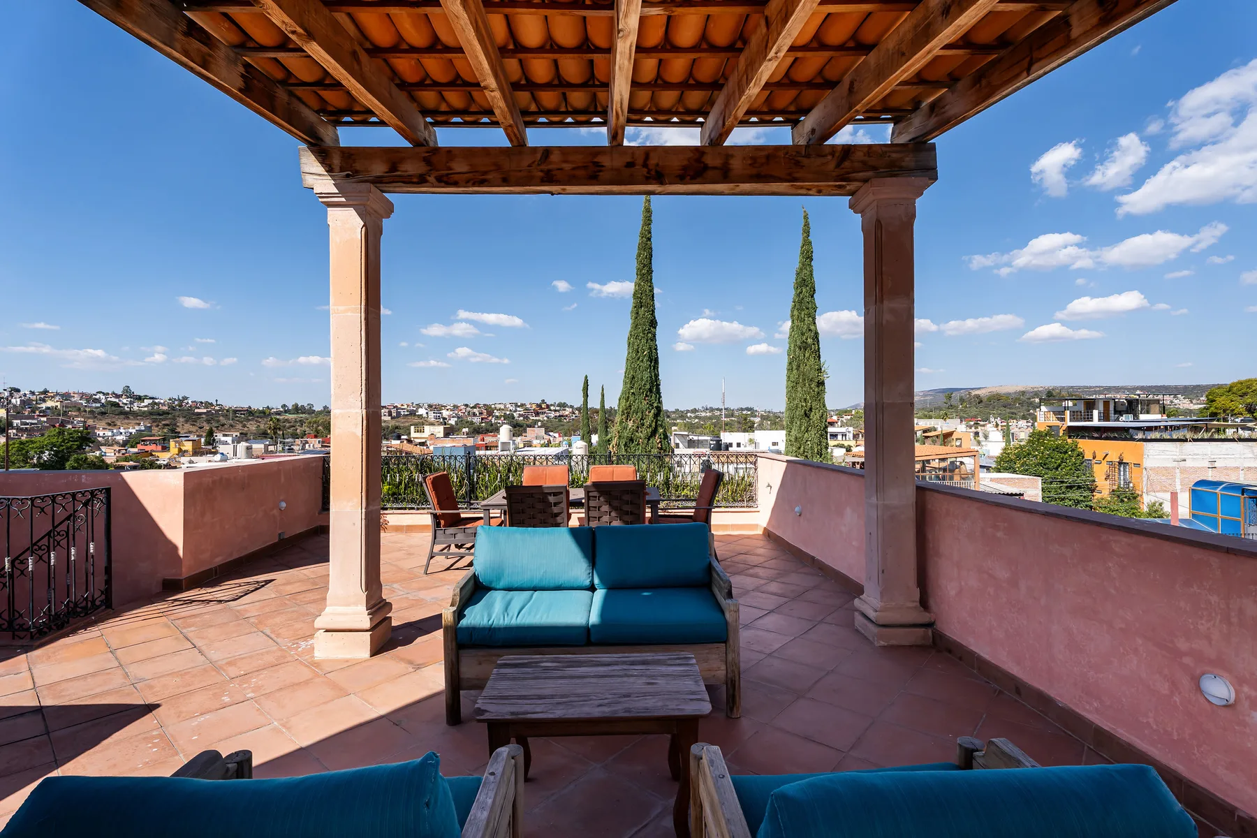 A covered rooftop terrace with blue seating and views across the surrounding city.