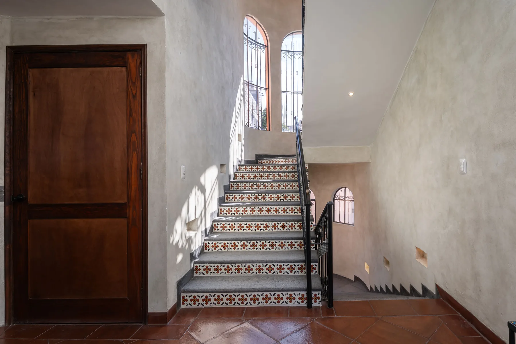 A tiled staircase rises beside a wooden door in a bright interior hallway.