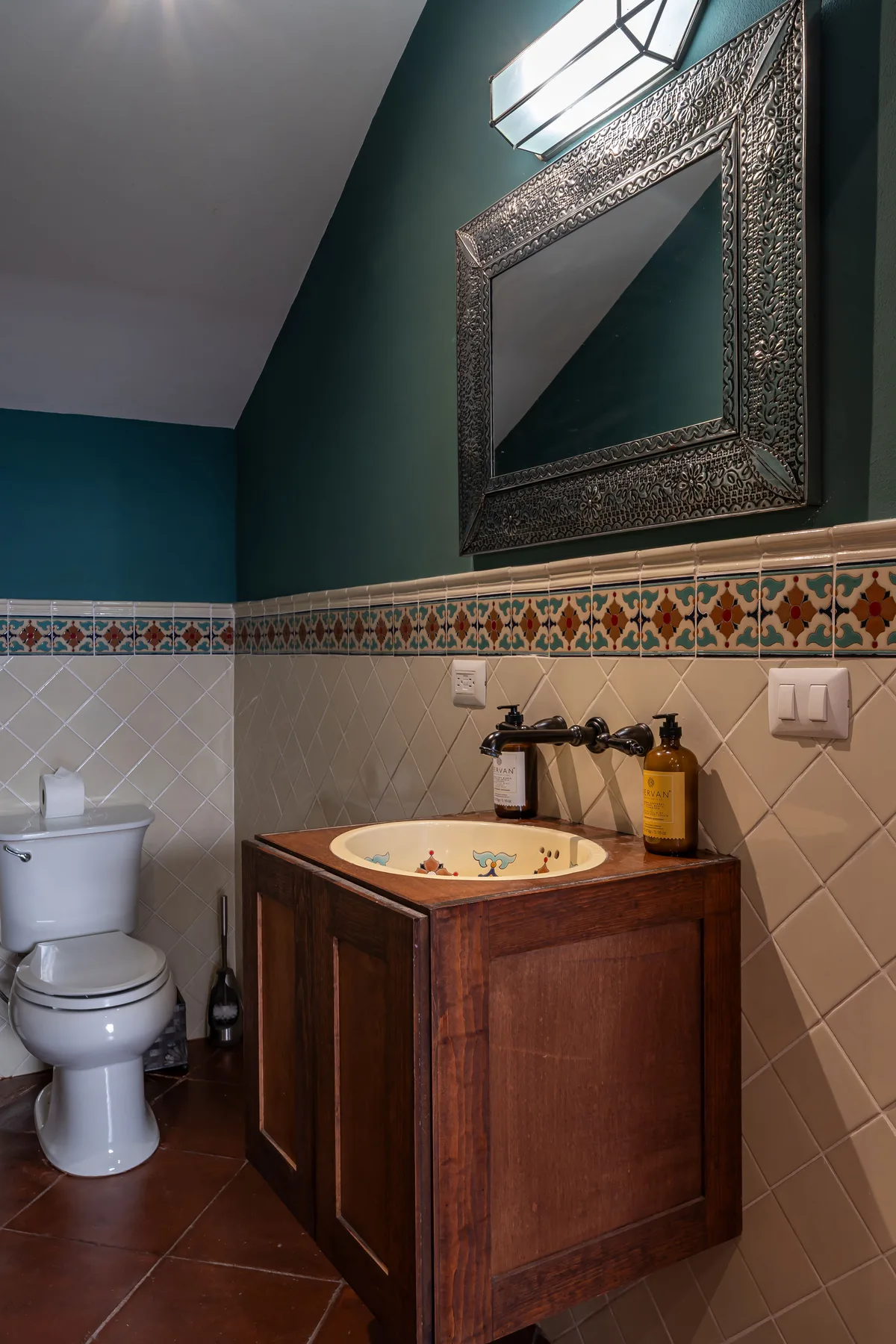 A bathroom with a wooden vanity, sink, and toilet beneath a framed mirror.