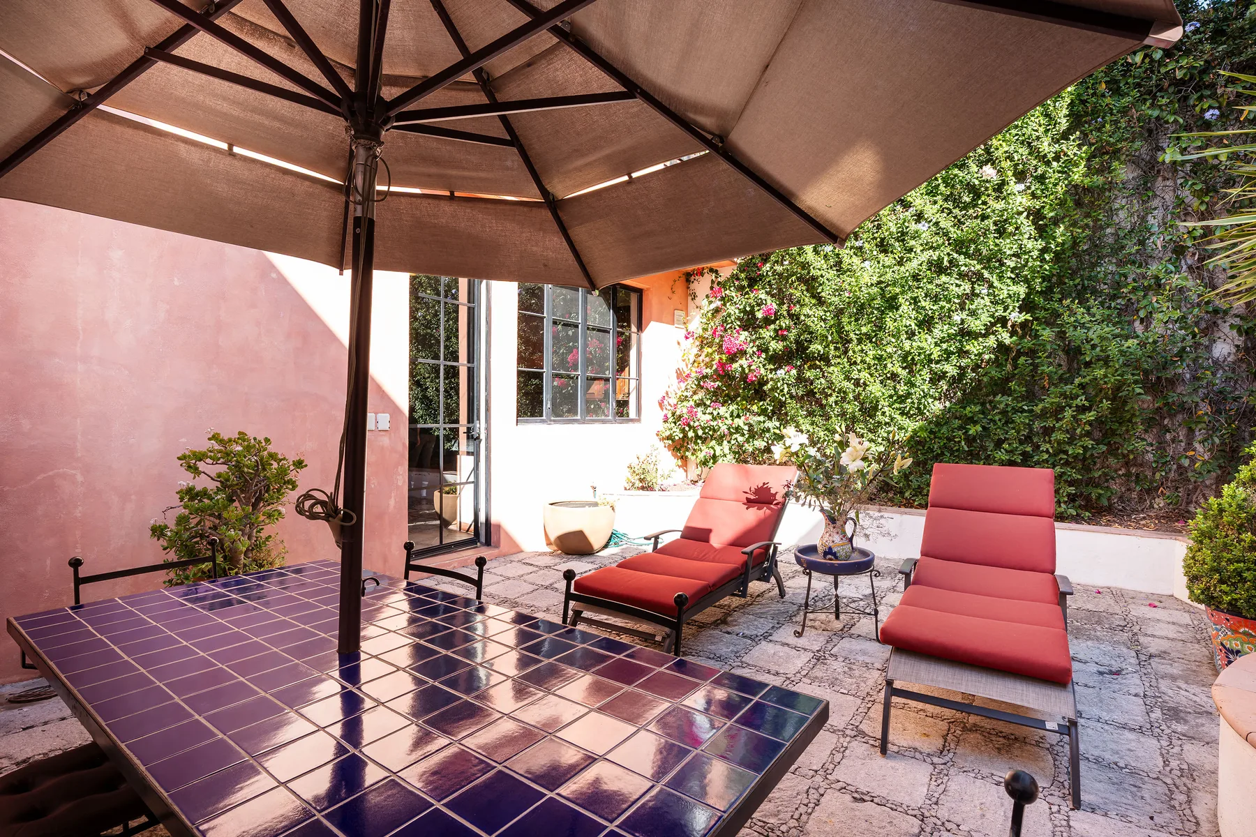 An outdoor patio with cushioned lounge seating beneath a large umbrella.