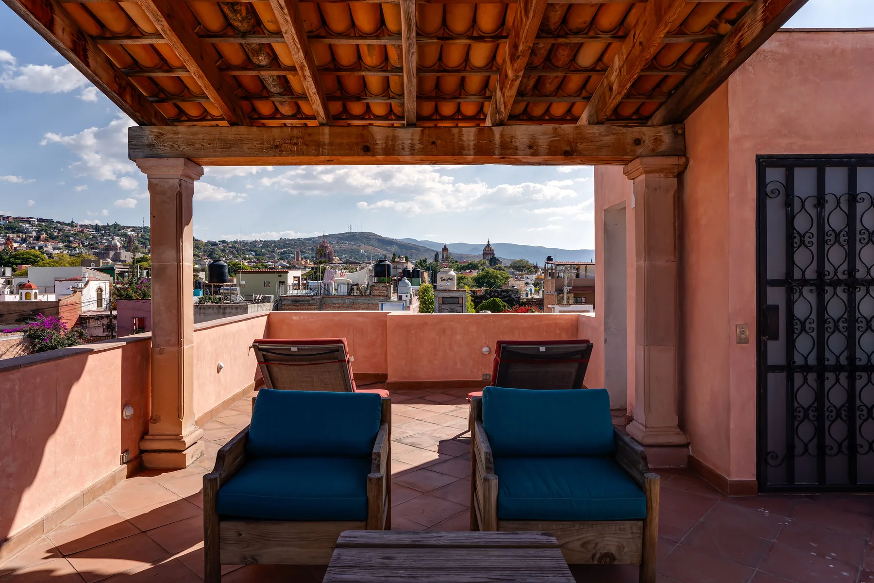 A covered rooftop terrace with seating overlooks a hillside town.