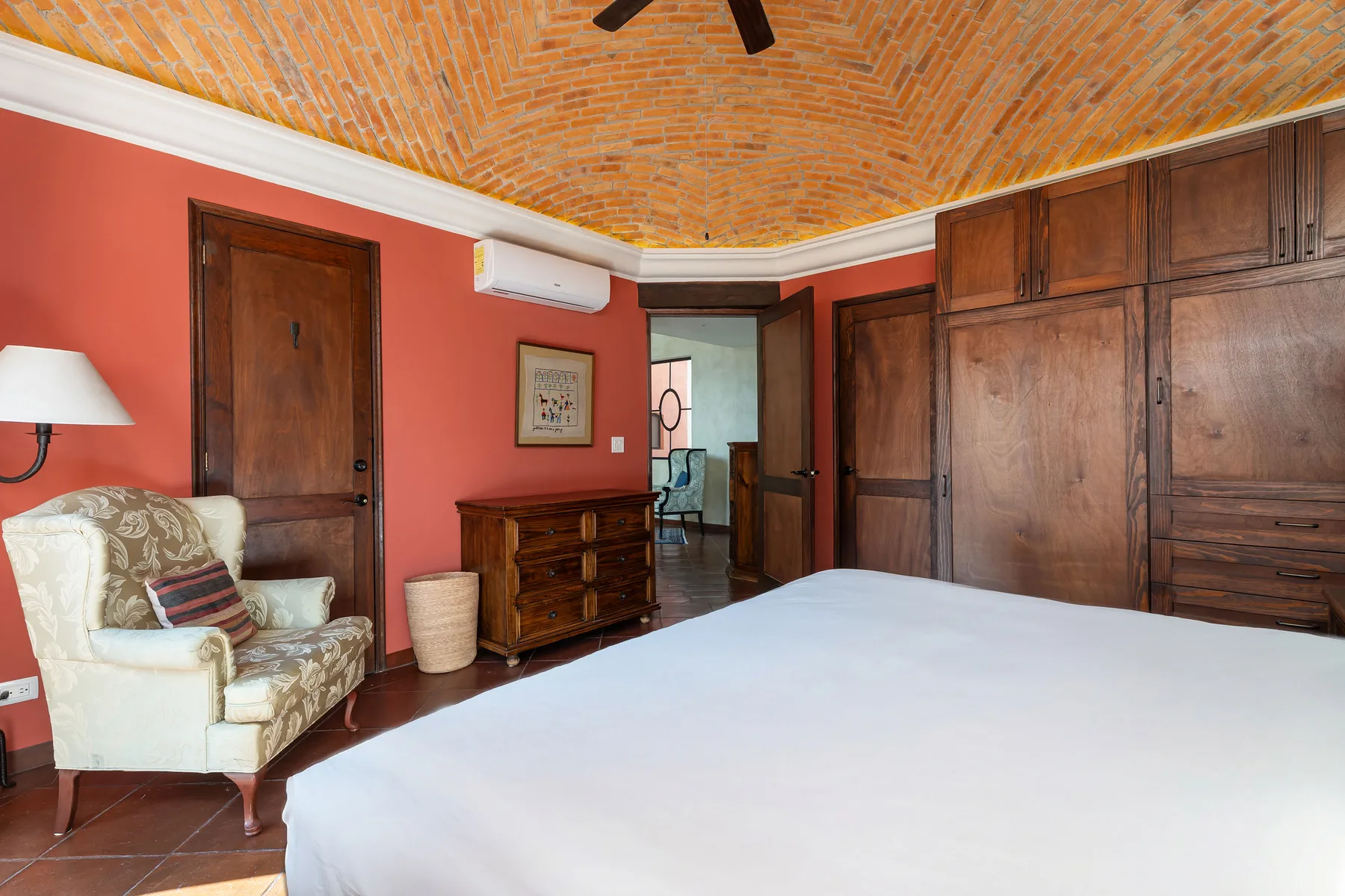 A bedroom with a large bed, wooden storage cabinets, and an upholstered armchair.