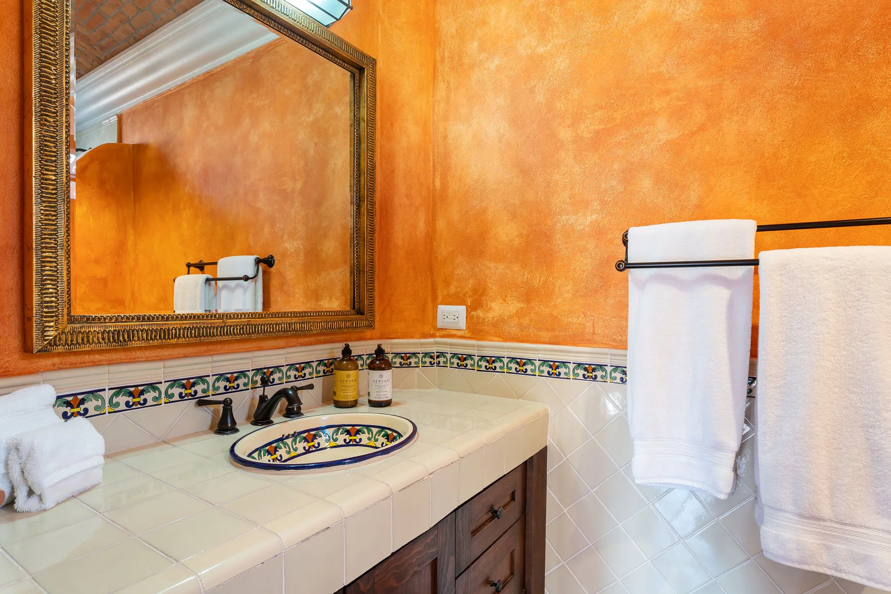 A bathroom vanity with a decorative tiled sink and a large wall mirror.
