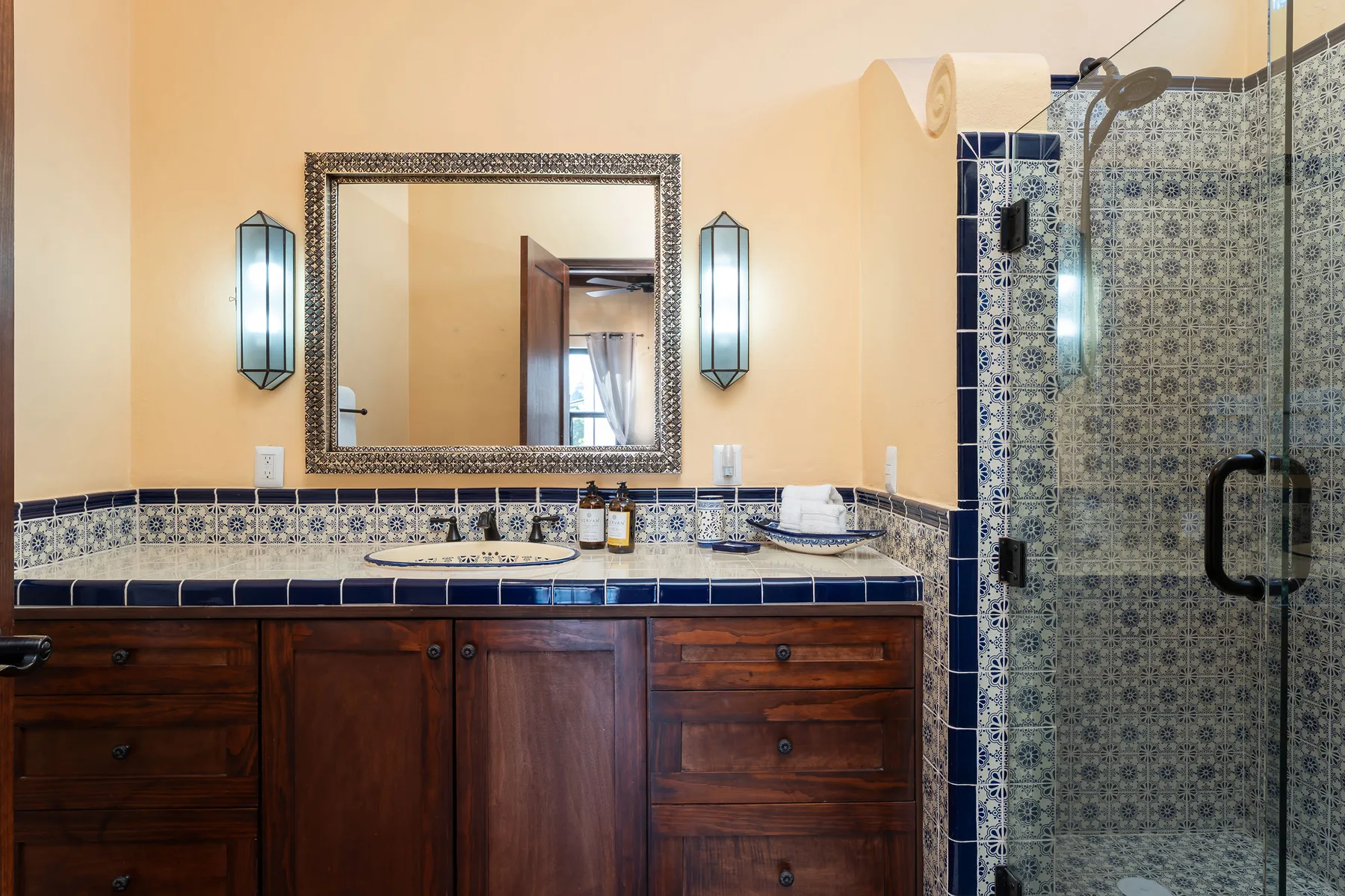 A bathroom vanity with a mirror and a tiled shower.