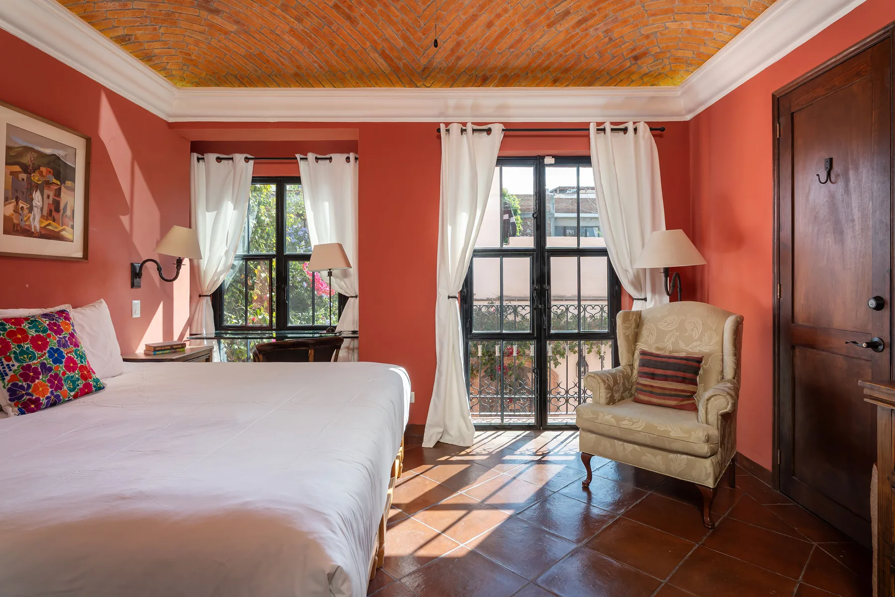 A bedroom with a bed, curtained windows, and an upholstered armchair.
