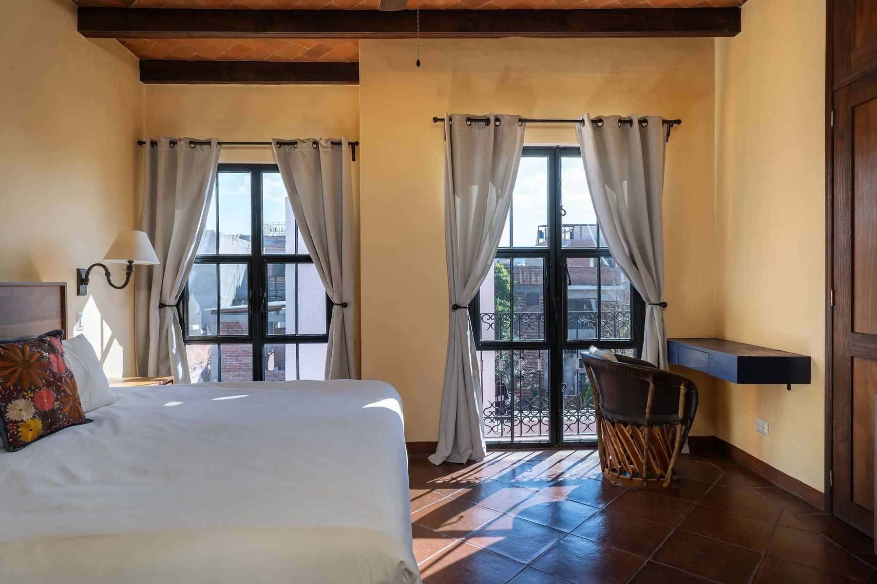 A bedroom with a bed, tall windows, and a small desk.