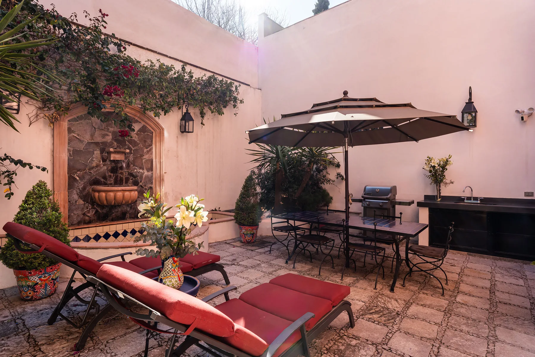 A pink-walled courtyard patio with a fountain, table seating, and an umbrella.