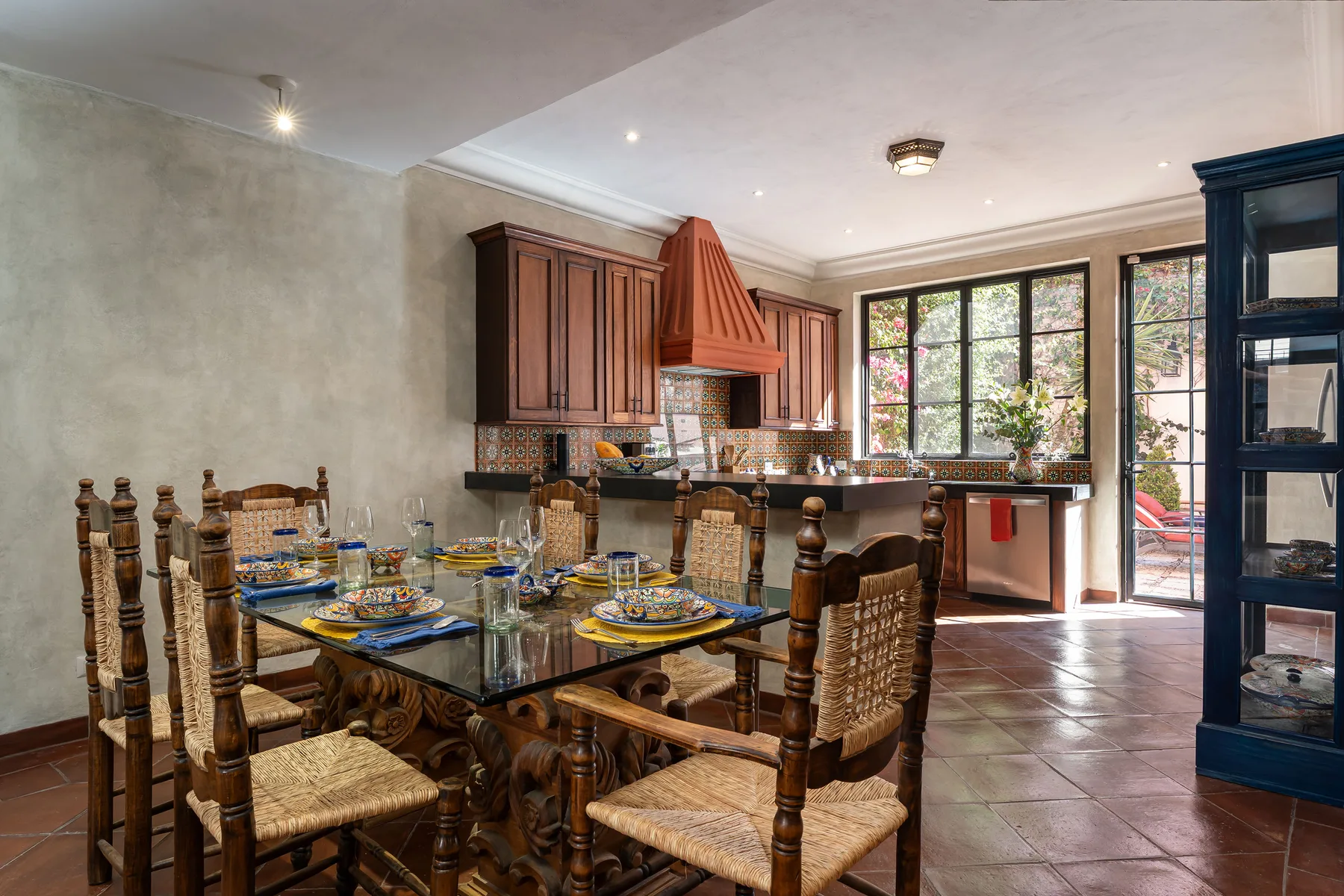 A dining area with a set table beside a kitchen and large windows.