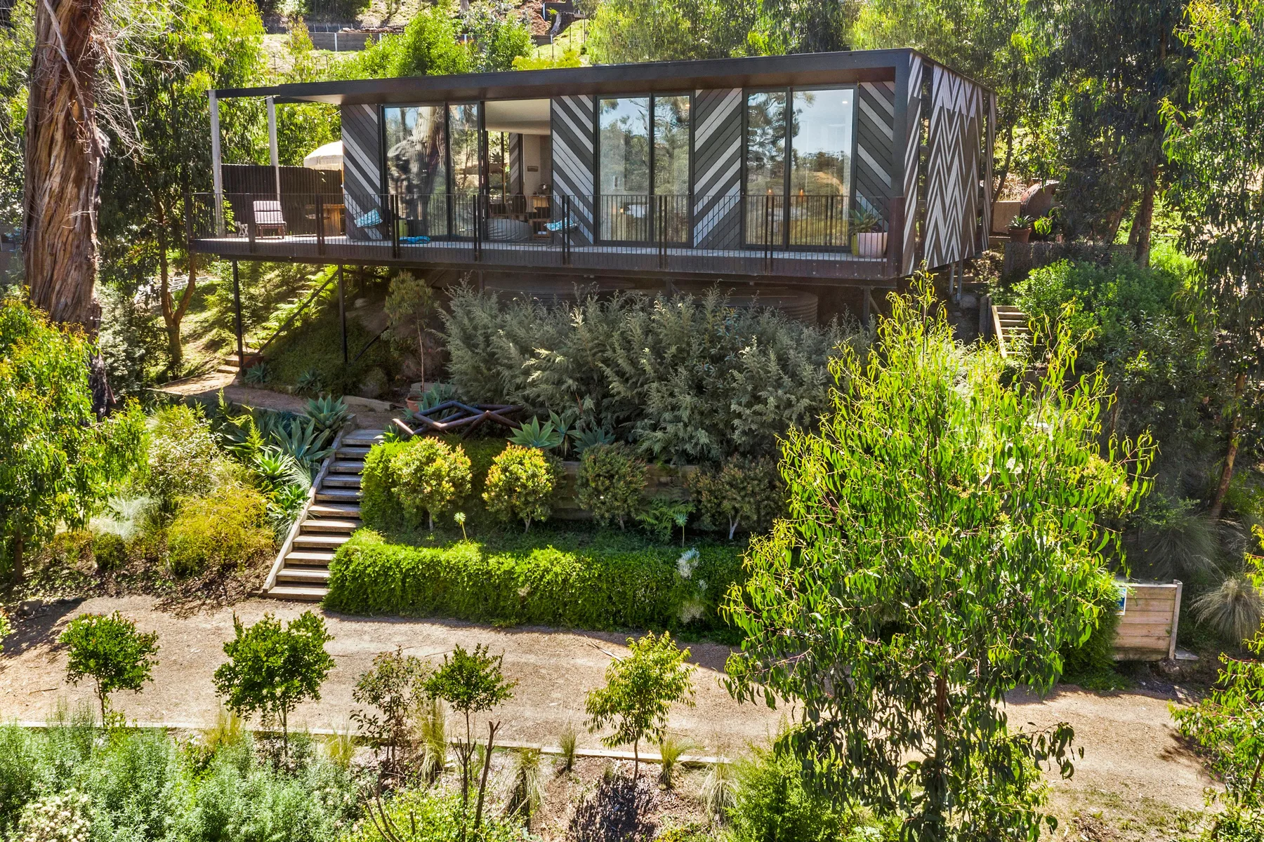 Una casa moderna con fachada de vidrio se encuentra entre árboles sobre un jardín ajardinado.
