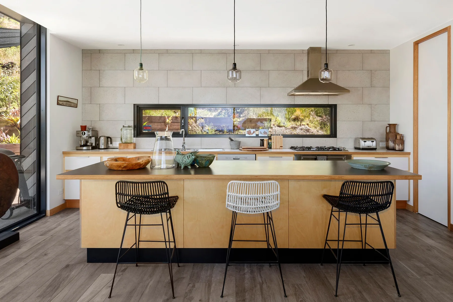 Una cocina moderna con una isla central y taburetes frente a las ventanas.