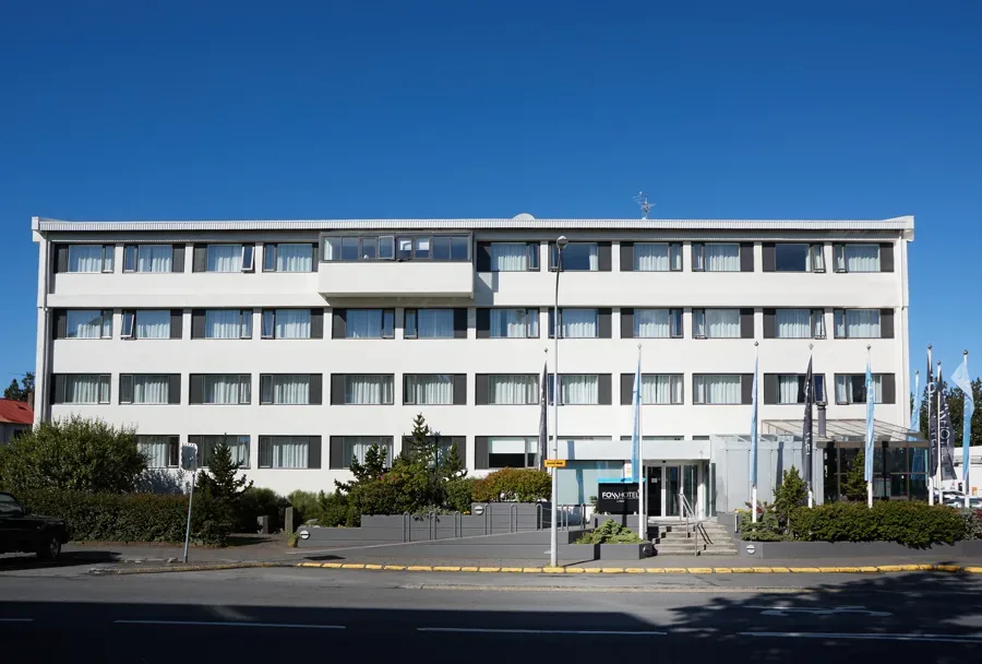 Espacio representativo del hotel: Un edificio blanco de varias plantas con filas de ventanas da a una calle pavimentada.