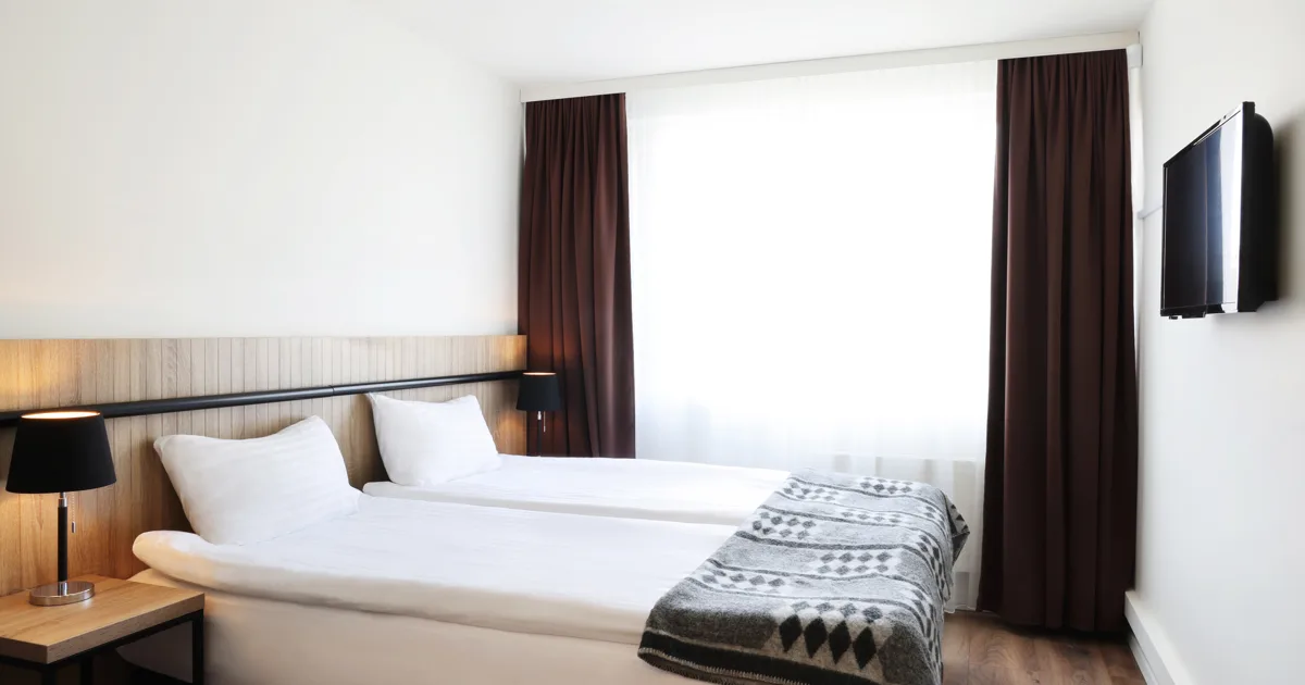 Espacio representativo del hotel: Un dormitorio de hotel con dos camas, cortinas oscuras y un televisor en la pared.