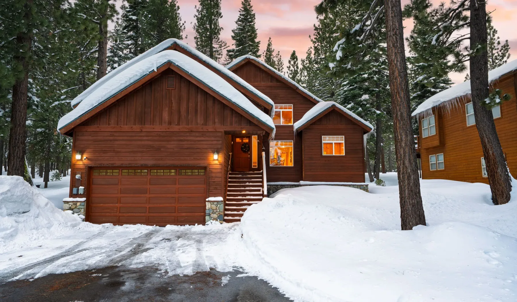 Cabañas de madera cubiertas de nieve entre pinos al atardecer.
