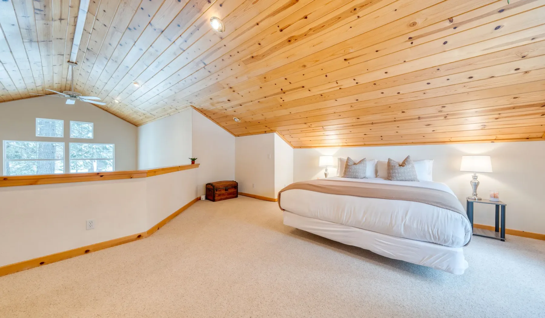 Un dormitorio con una cama bajo un techo inclinado de madera y ventanas.