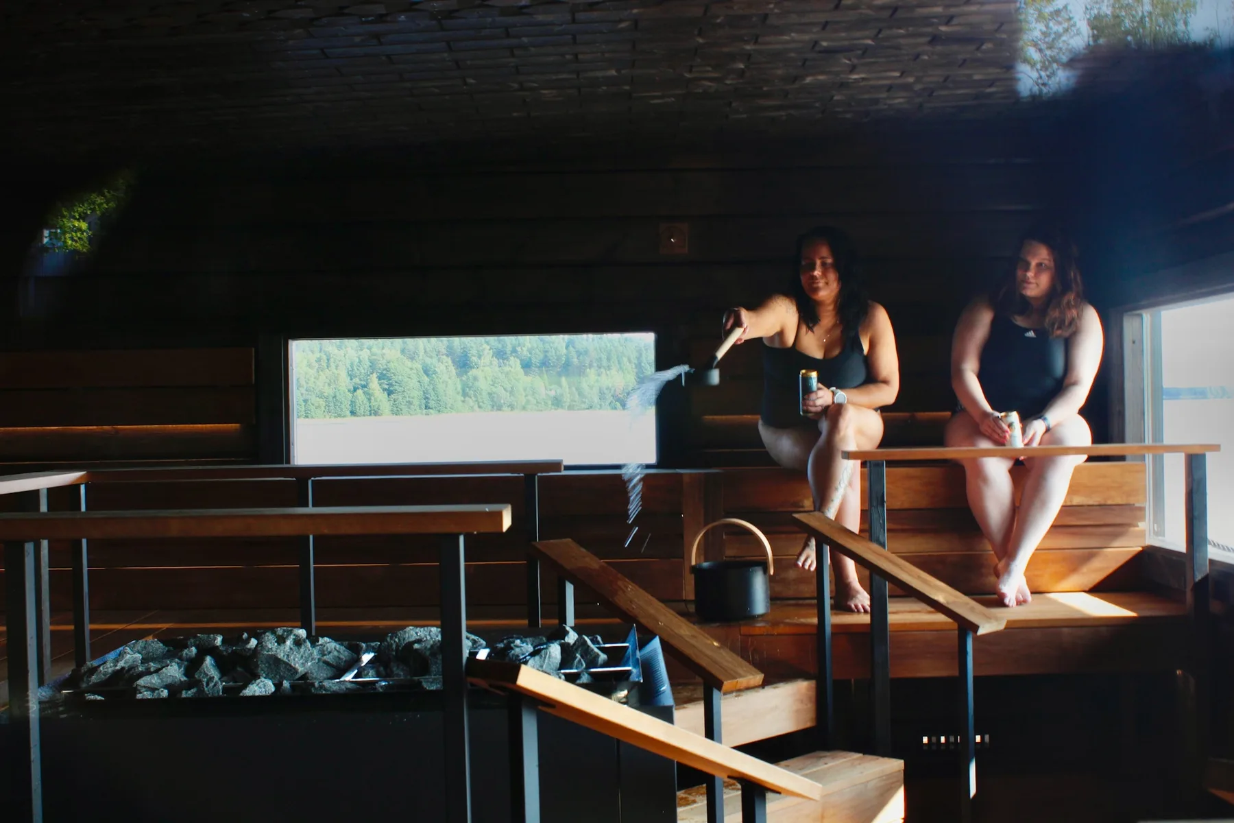 Representative hotel space: A dim sauna room with two people seated beside a heated stone area.