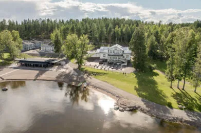 Representative hotel space: A lakeside building and outdoor seating sit beside a wooded shoreline.