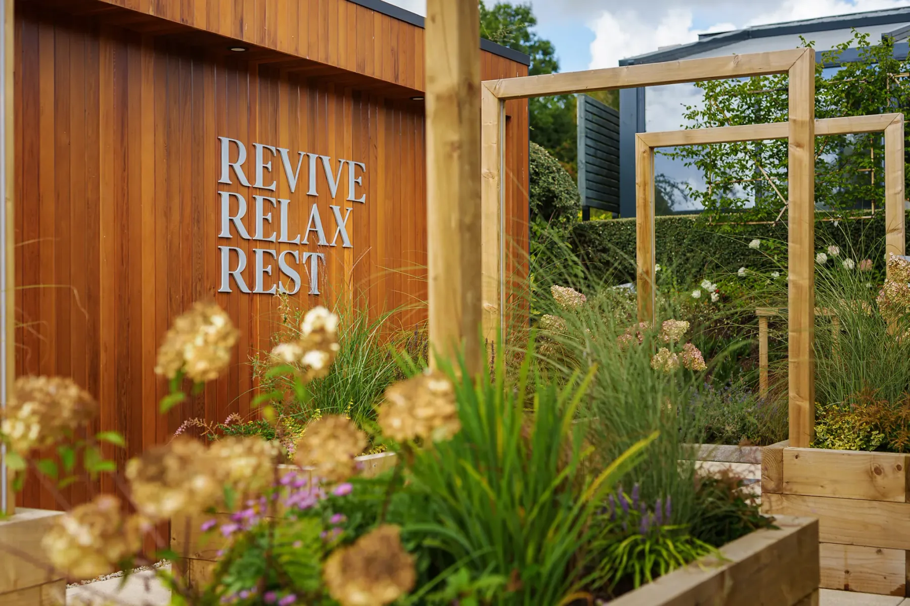 Representative hotel space: An outdoor garden path passes wooden frames beside a planted bed.