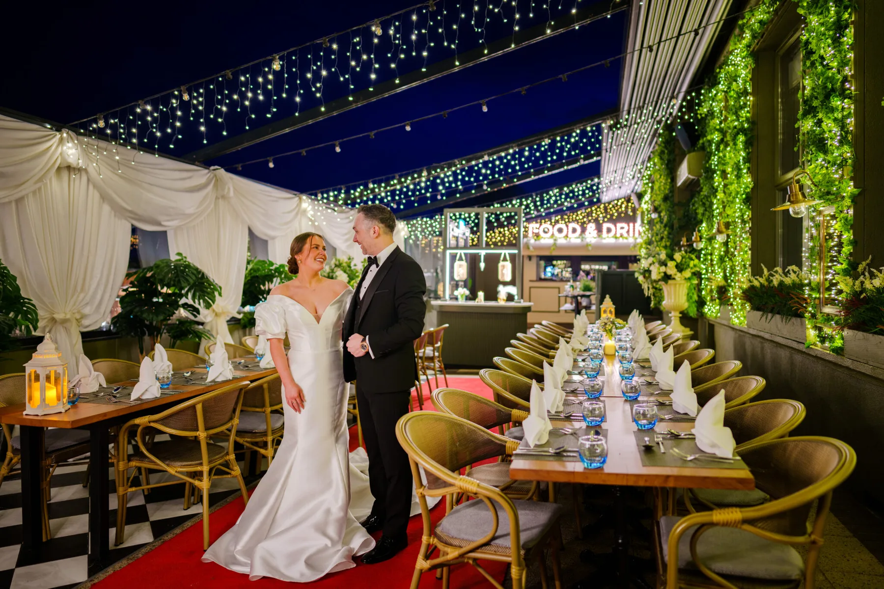 Representative hotel space: A wedding couple stands beside a long dining table under string lights.