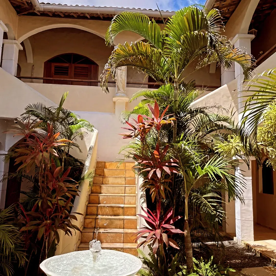 Espacio representativo del hotel: Una escalera del patio asciende entre exuberantes plantas tropicales bajo un balcón abierto.