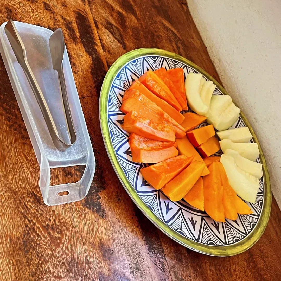 Espacio representativo del hotel: Un plato estampado contiene papaya y fruta clara en rodajas junto a unas pinzas.