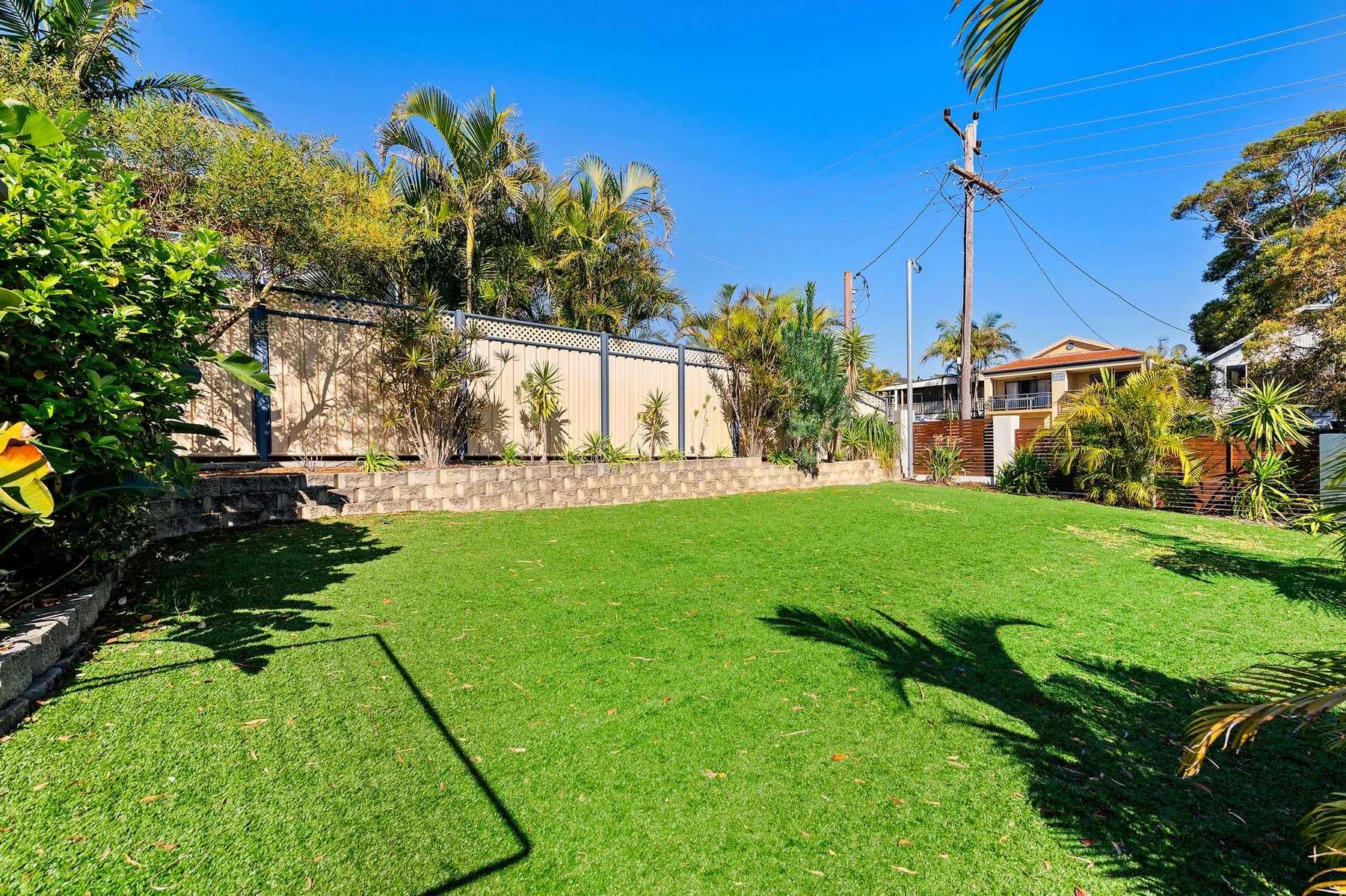 Un patio exterior con césped, plantas frondosas y una cerca.