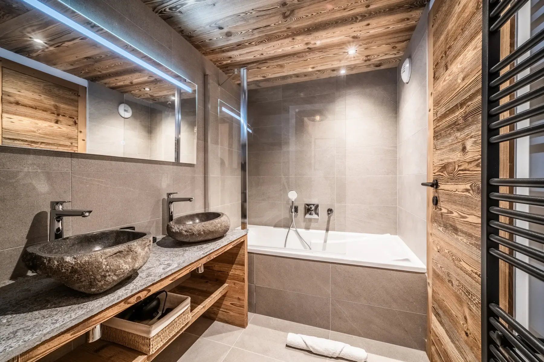 Un baño con bañera, dos lavabos sobre encimera y acabados de madera.