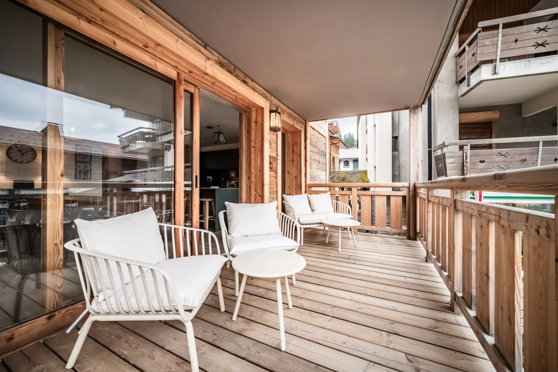 Un balcón de madera con asientos blancos y puertas de vidrio frente a un patio.