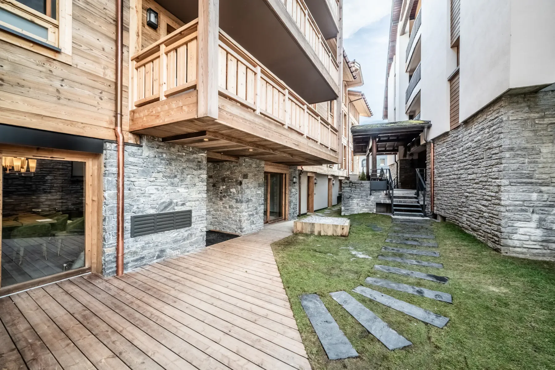 Zona común: Un patio con una terraza de madera, césped y losas entre los edificios.