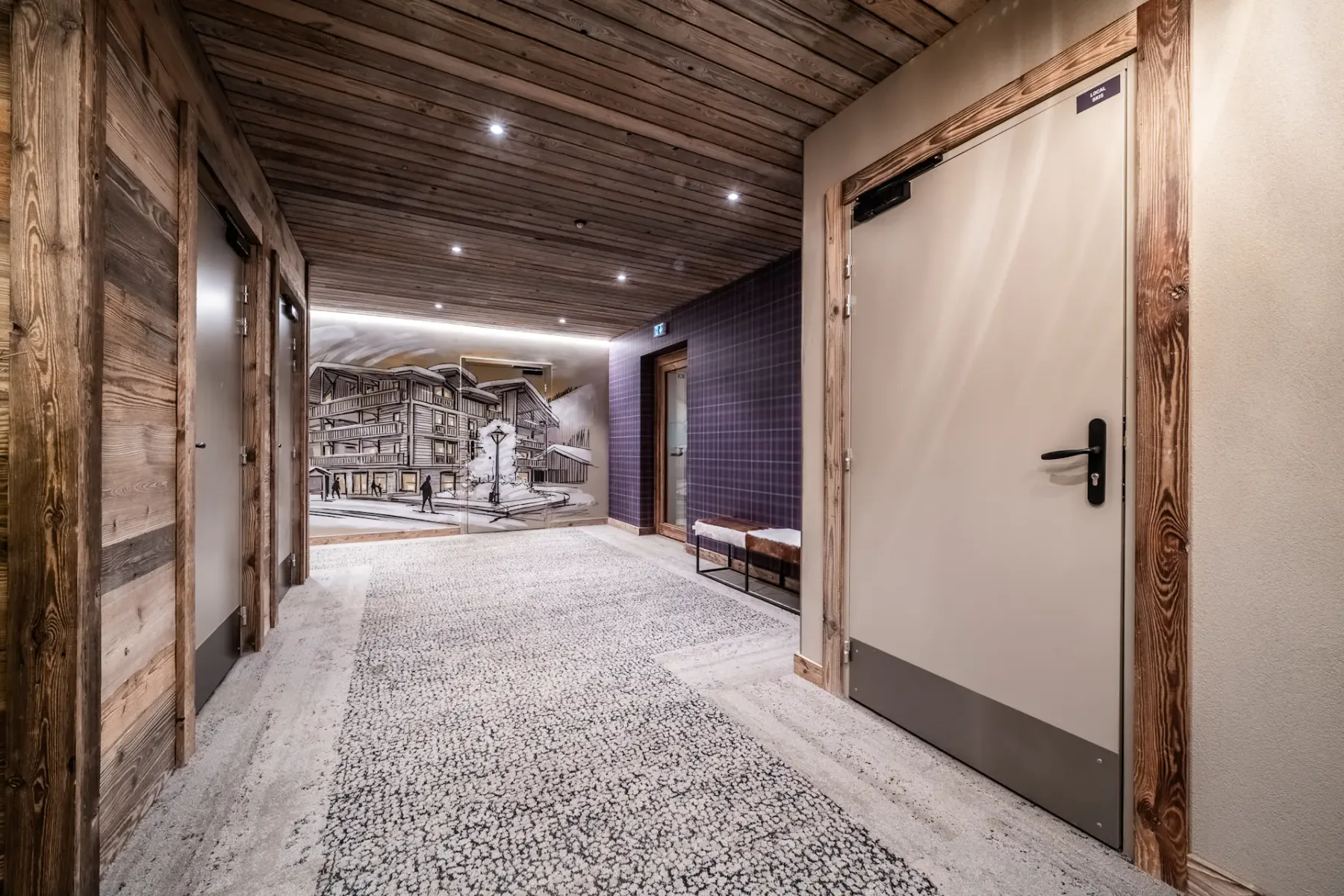 Zona común: Un pasillo revestido de madera con puertas y un mural al fondo.