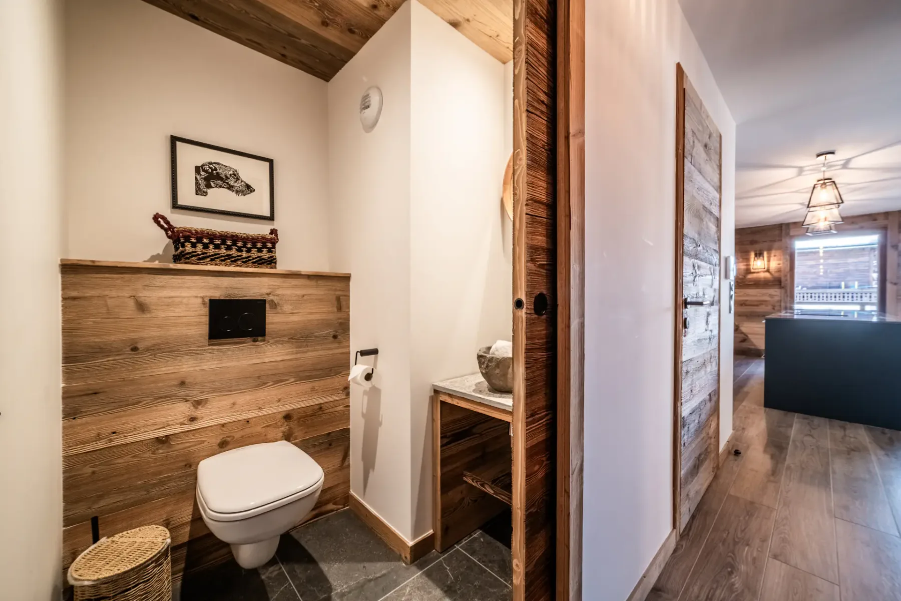 Un baño con inodoro, pared revestida de madera y un lavabo pequeño.