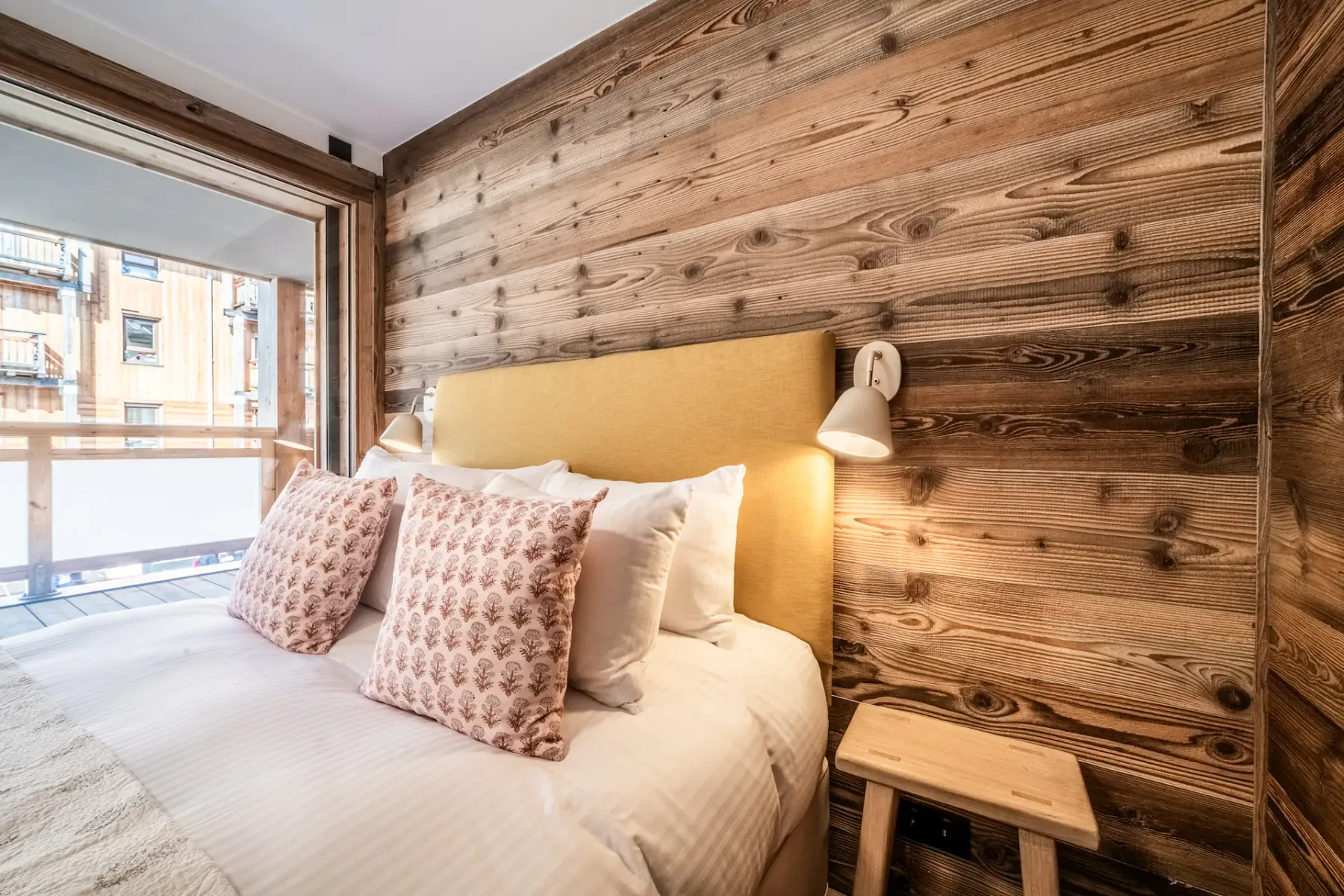 Un dormitorio con una cama junto a una ventana grande y paredes revestidas de madera.