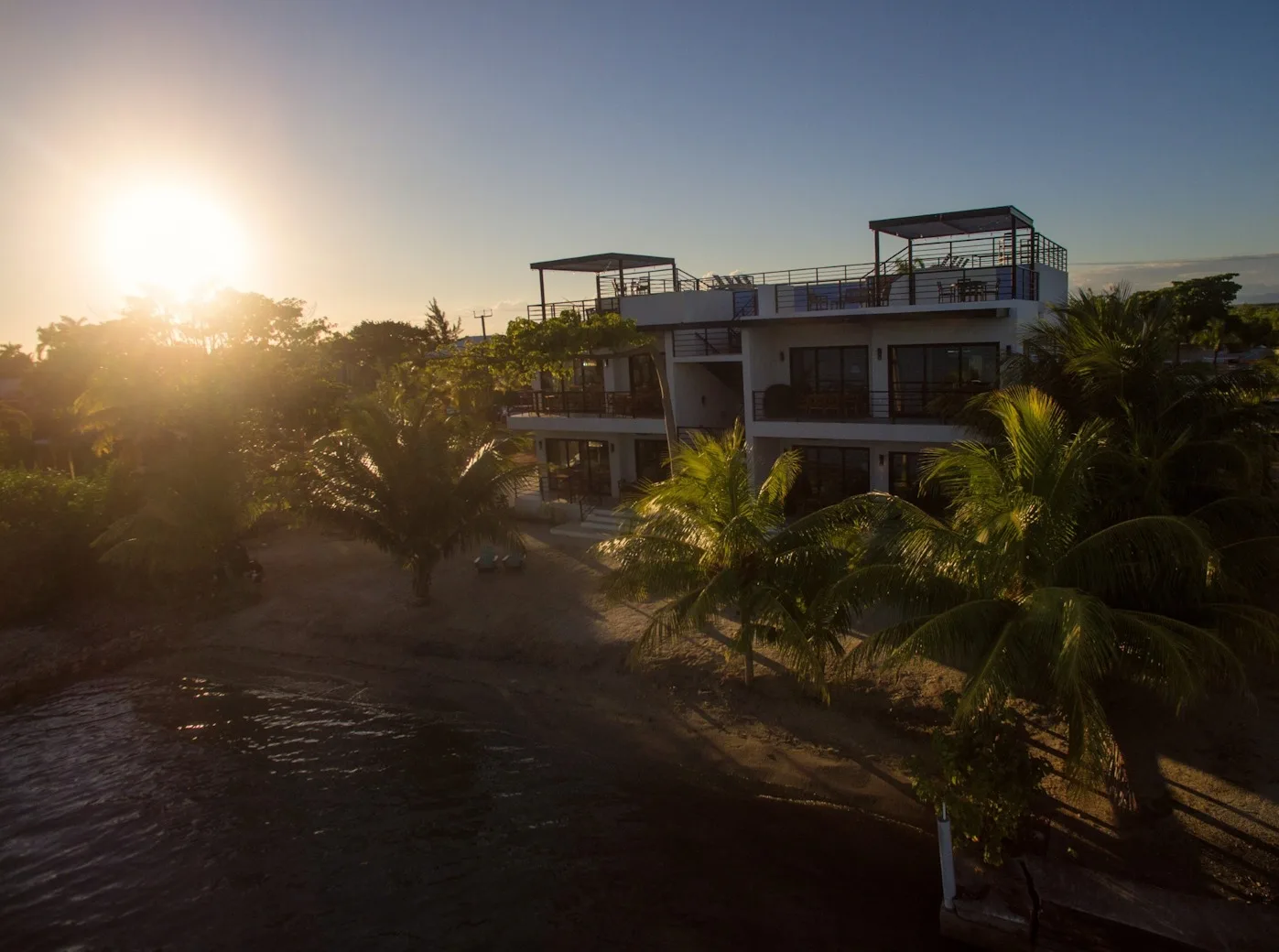 Zona común: Un edificio moderno se alza entre palmeras junto al agua al atardecer.