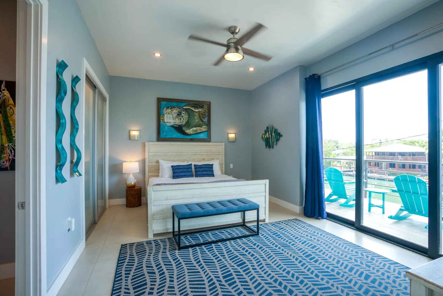 Un dormitorio con una cama, detalles azules y puertas corredizas de vidrio hacia un balcón.