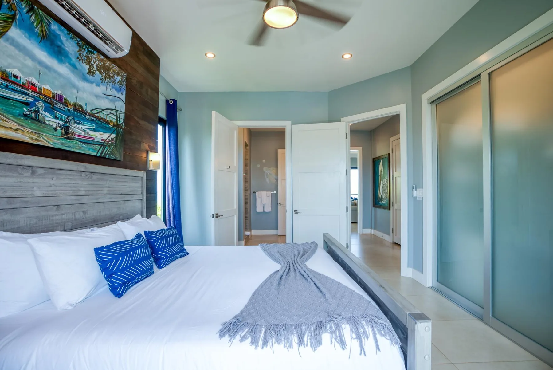 Un dormitorio con ropa de cama blanca, cojines azules y puertas corredizas de vidrio.