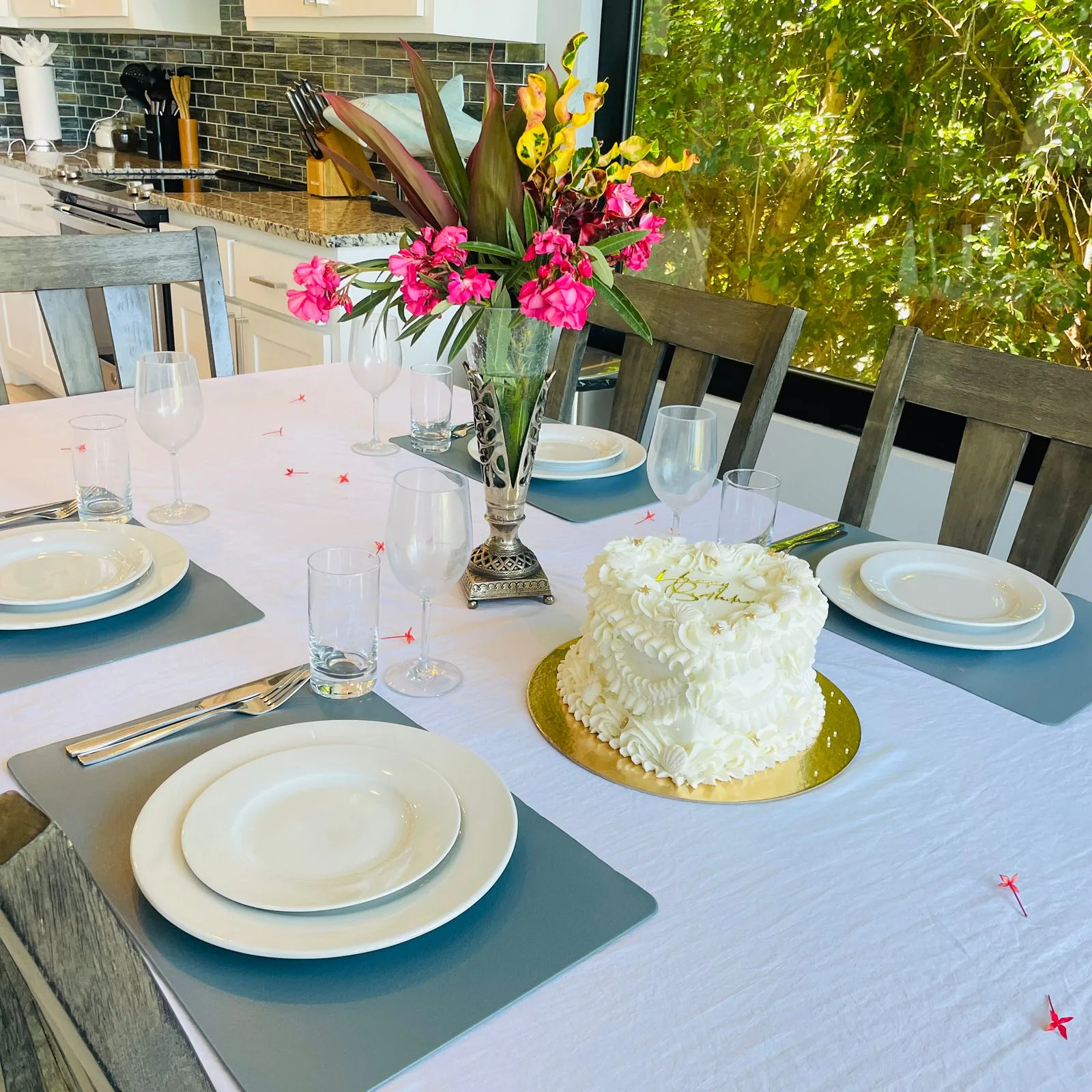 Una mesa de comedor está puesta con platos, vasos, un arreglo floral y un pastel.