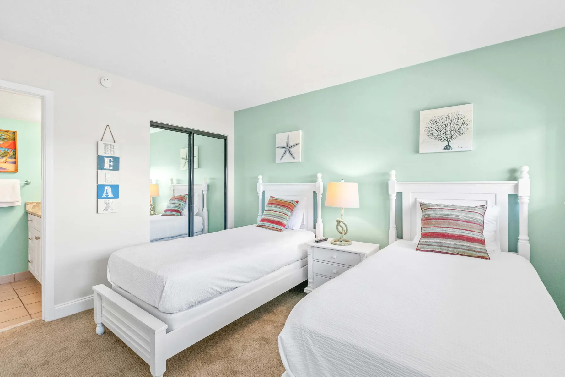 Un dormitorio luminoso con dos camas, mesitas de noche y una pared verde claro.