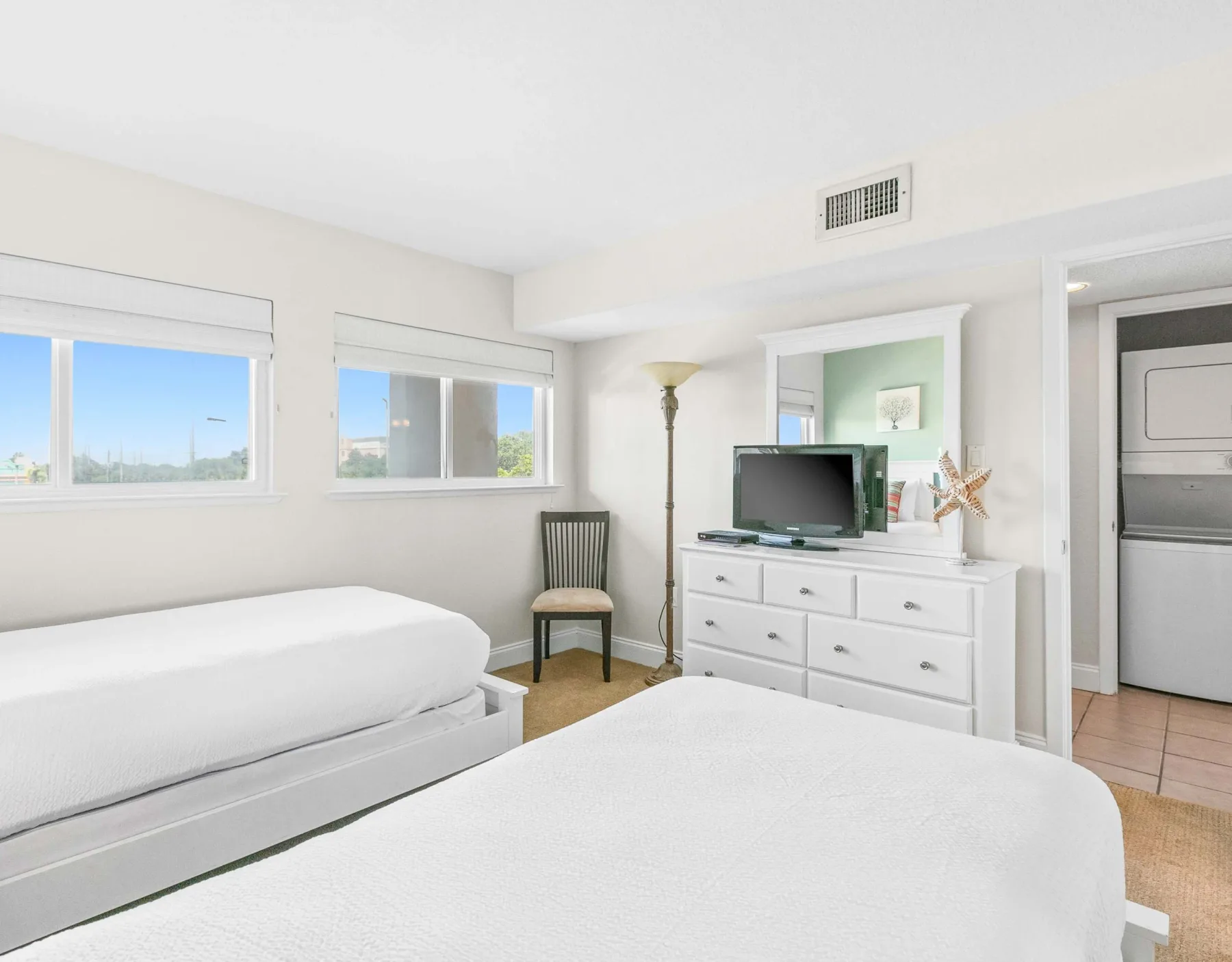 Un dormitorio luminoso con dos camas, una cómoda y un televisor.