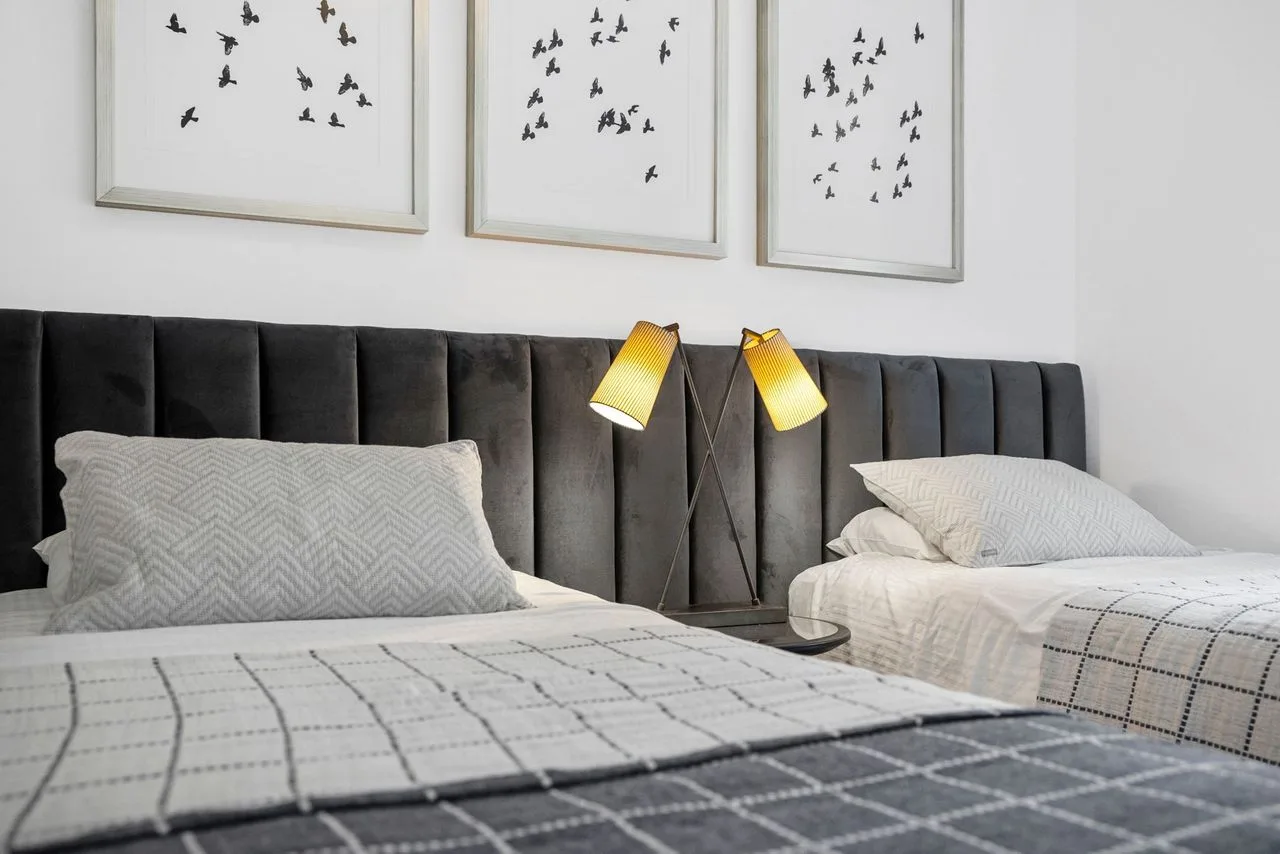 A bedroom with two beds, a dark upholstered headboard, and framed prints.