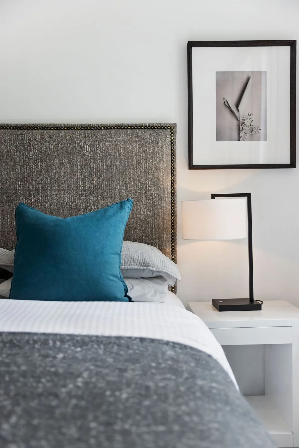 A bedroom with a bed, teal pillow, and bedside lamp.