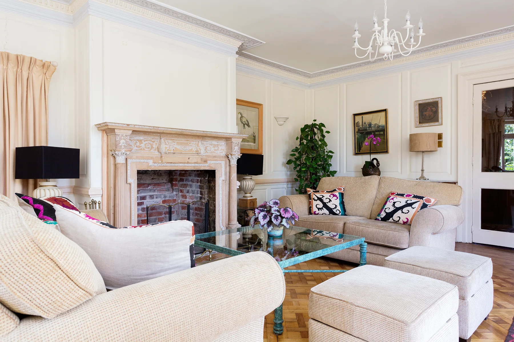 Una sala luminosa con asientos tapizados, una mesa de centro de vidrio y una chimenea ornamentada.