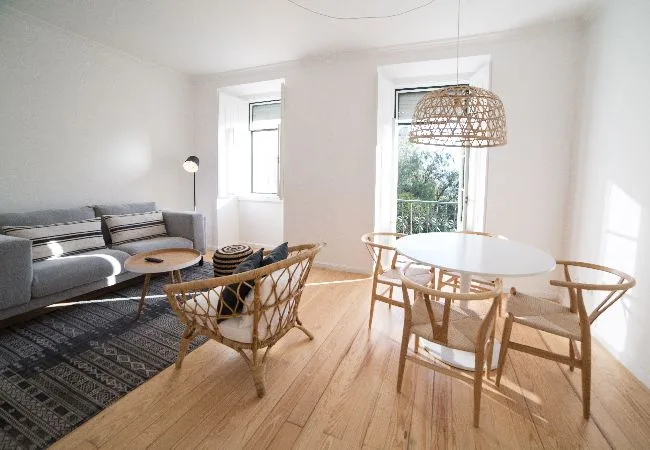 A bright living and dining area with a sofa, table, and woven pendant light.