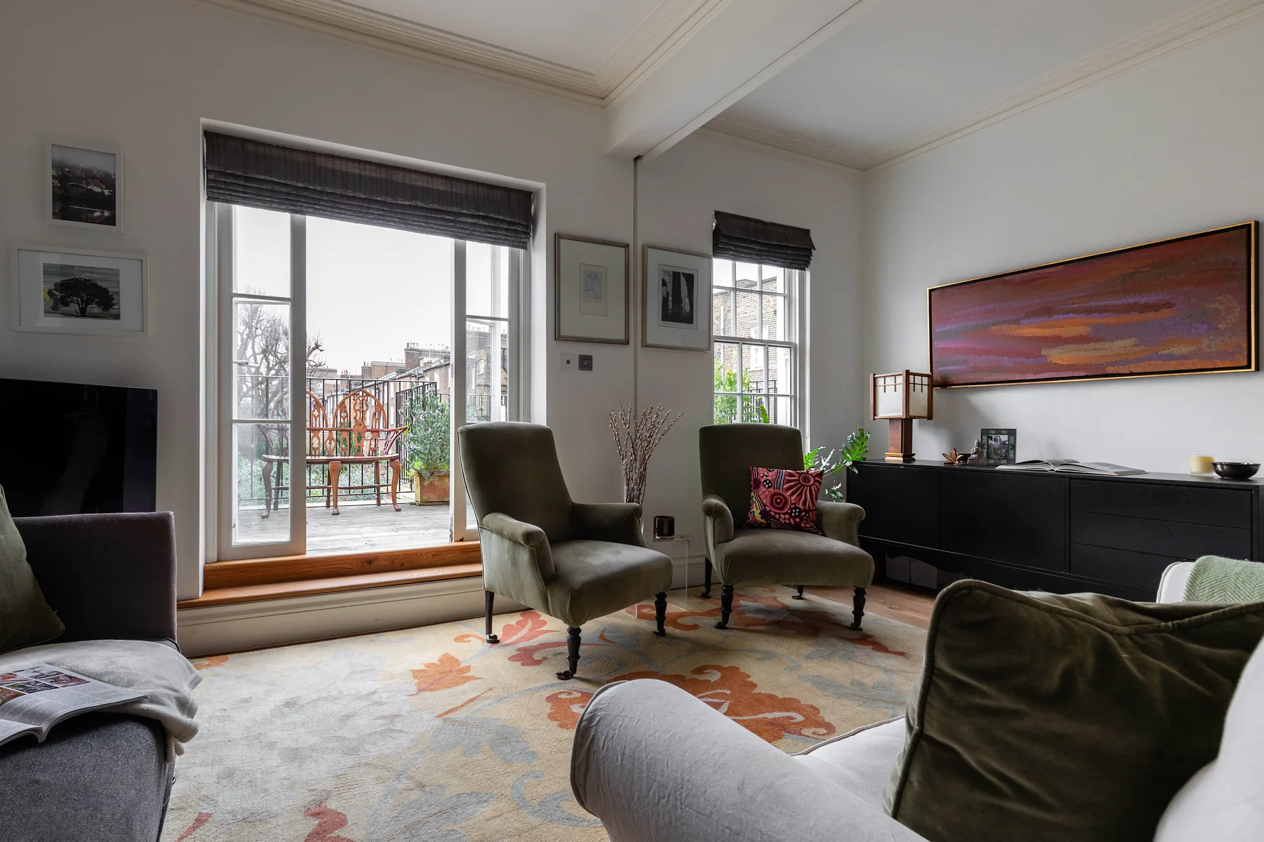 A living room with seating, a large rug, and windows overlooking a balcony.