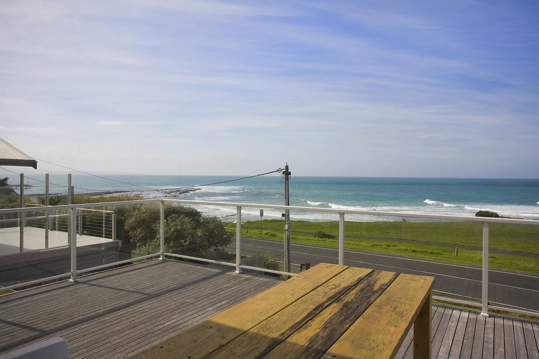 A wooden deck overlooks a grassy coastal strip and the ocean.